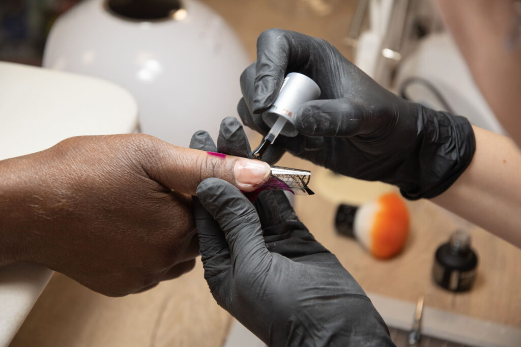 manicurist doing nail extensions to dark skinned