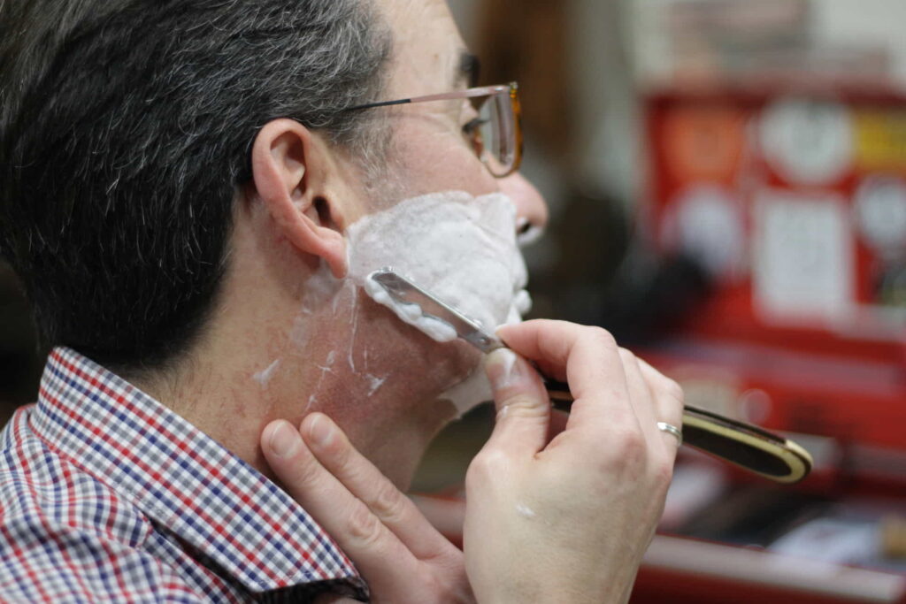 Close-up of a skilled shave using a straight razor, highlighting the precision and care in the process