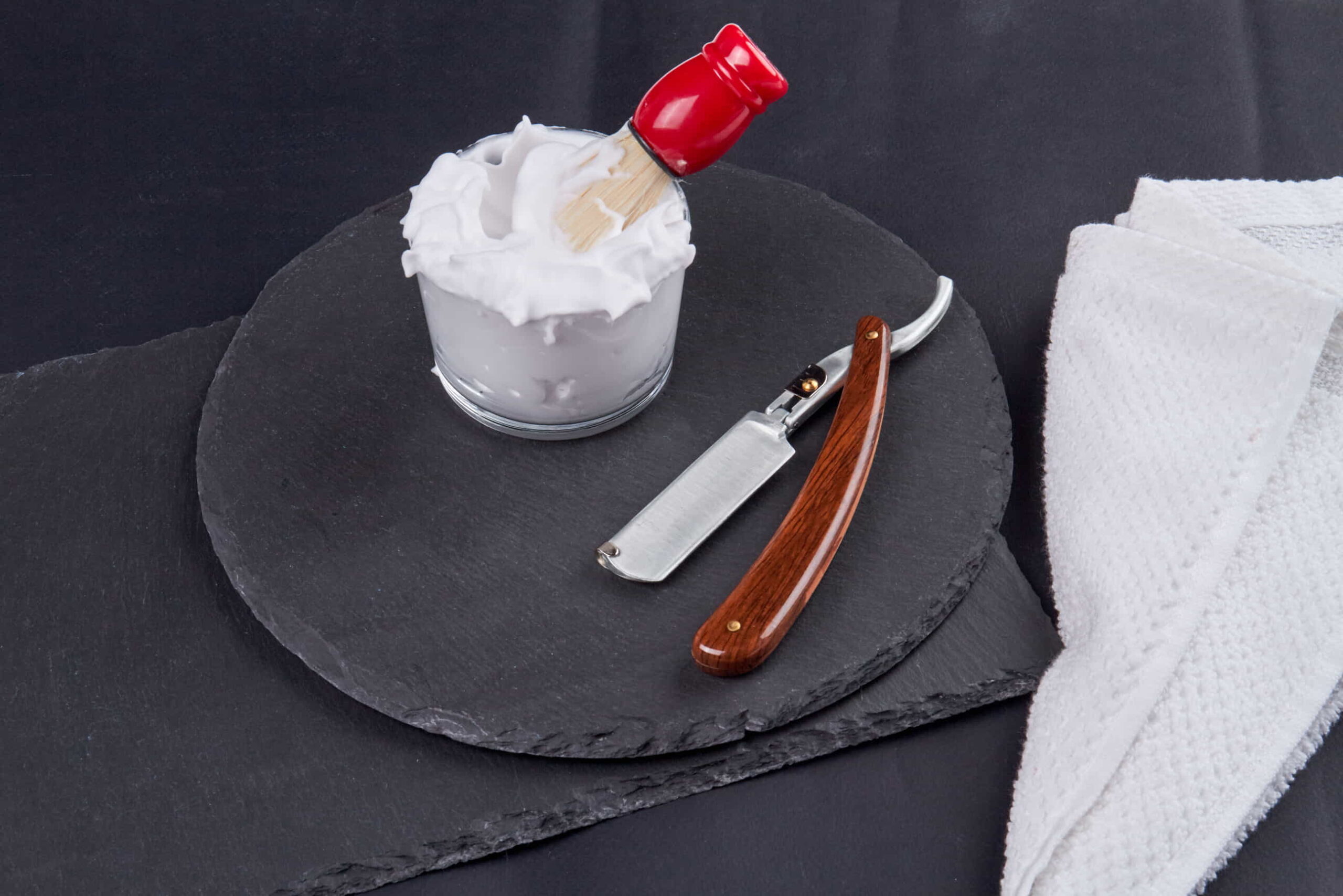 Elegant straight razor with wooden handle, placed beside classic shaving accessories
